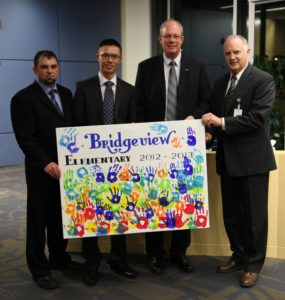 Bridgeview elementary school principal Andrew Shook (from left), Mainroad's Calvin Chan and Doug Bjornson and Surrey Board of Education chairperson Shawn Wilson with a thank-you poster from the students who, thanks to Mainroad, took swimming lessons this year. Every student who attended lessons “signed” the poster with their handprints.